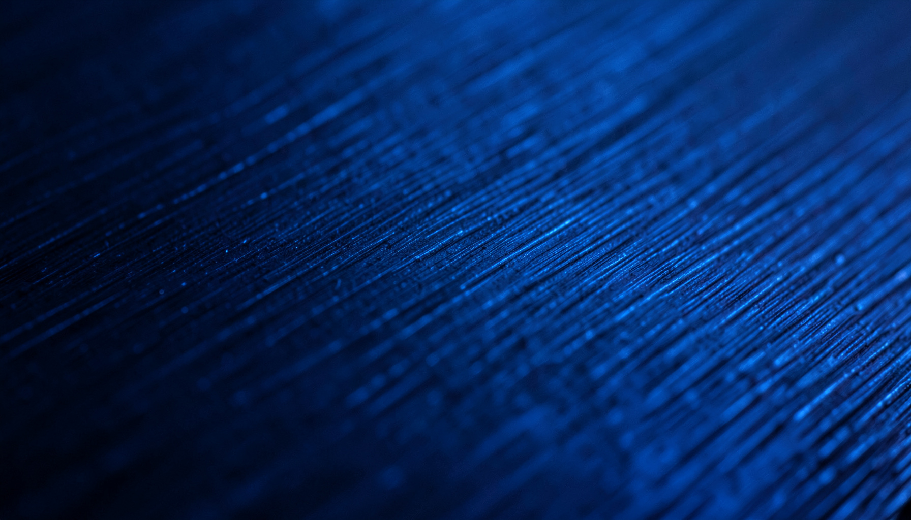 Extreme close-up of dark navy brushed metal surface with electric blue reflections