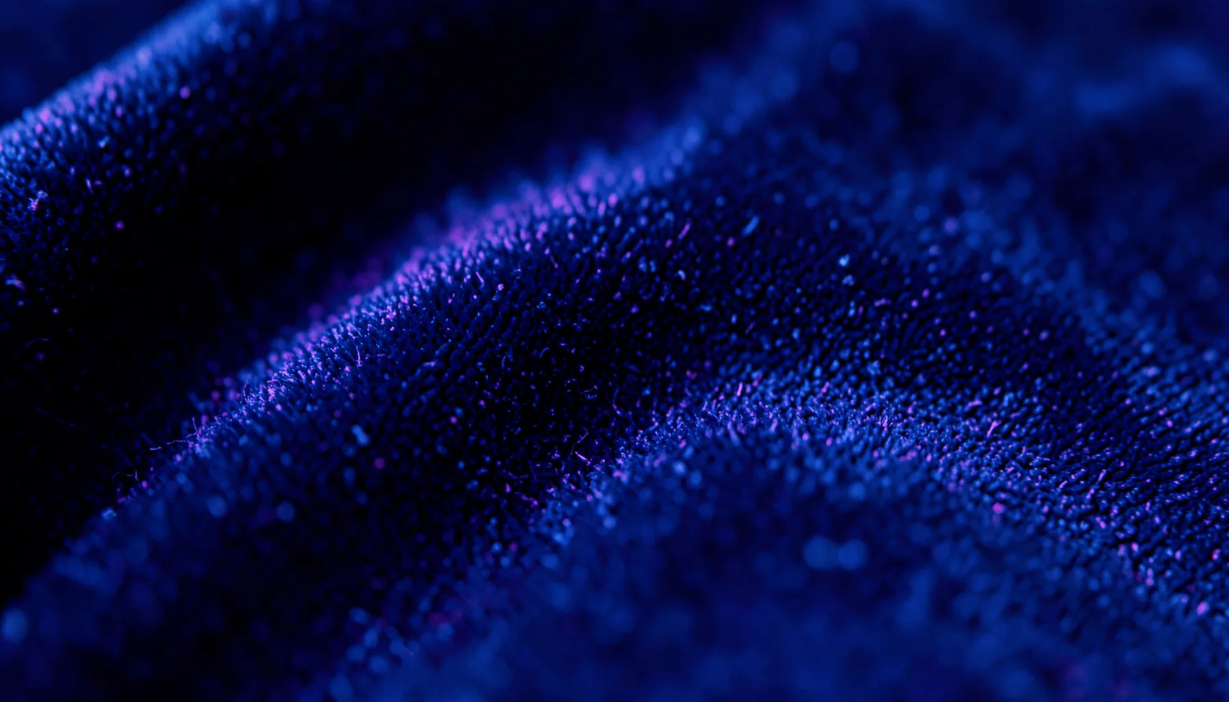 Extreme close-up of deep indigo velvet fabric texture with subtle neon purple highlights