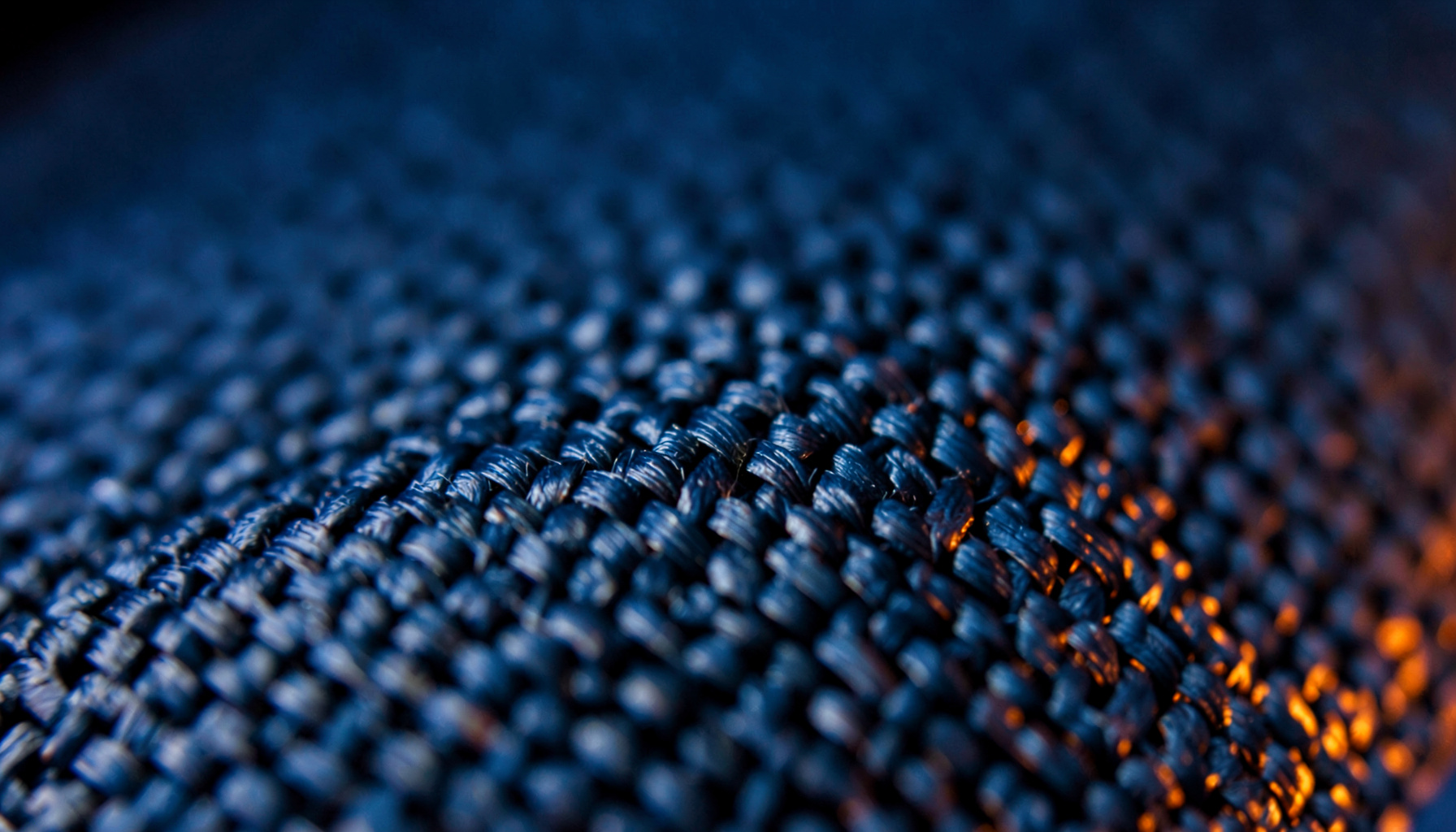 Extreme close-up of dark carbon fiber weave with hot orange edge glow