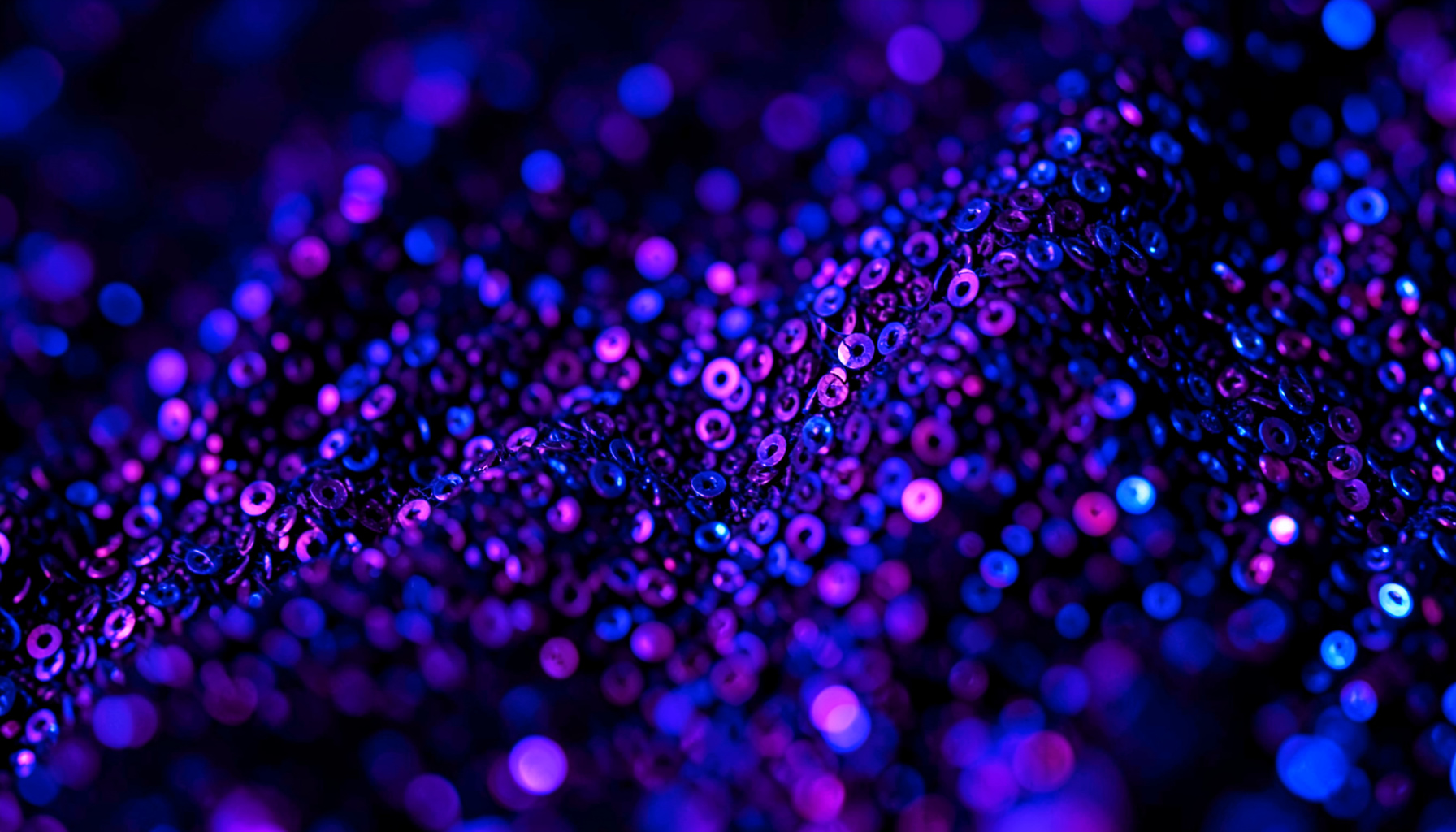 Extreme close-up of shimmering dark purple sequin fabric catching neon light