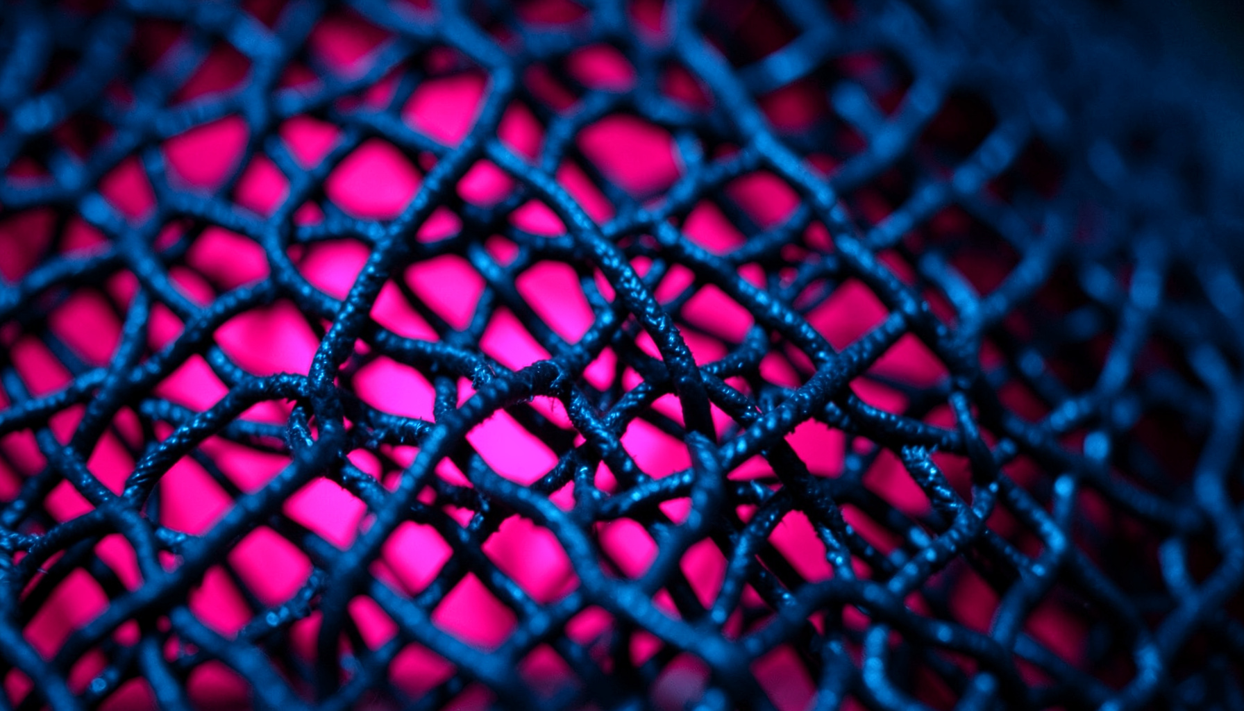 Extreme close-up of dark metallic mesh with hot pink backlight glow