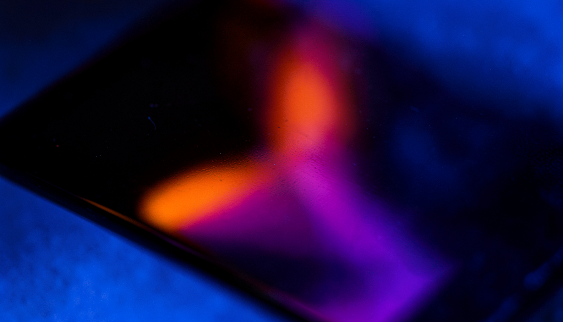 Extreme close-up of glossy black acrylic surface with neon orange and purple gradient reflection